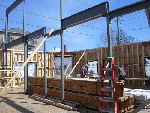 Chantier de construction avec poutres d'acier, charpente en bois, ouvriers et une échelle.