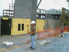 Construction worker using surveying equipment at a building site with concrete walls and safety barriers.