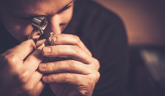 un uomo mentre osserva un anello con una lente di ingrandimento 