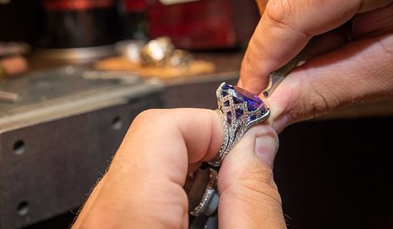Un gioielliere durante una lavorazione di un anello di con una pietra blu e dei brillanti