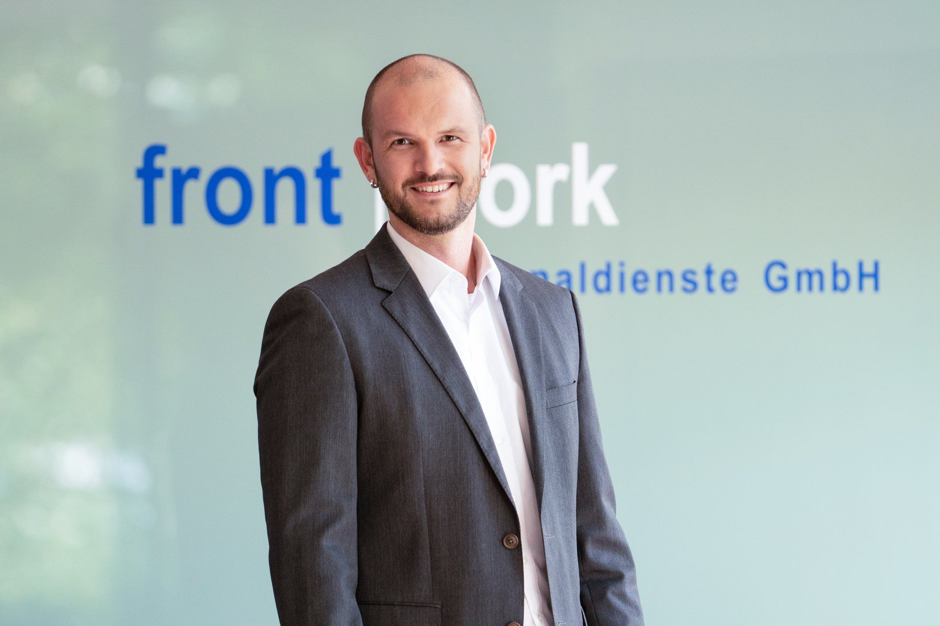 Ein Mann im Anzug steht vor einem Schild mit der Aufschrift „Front Work“