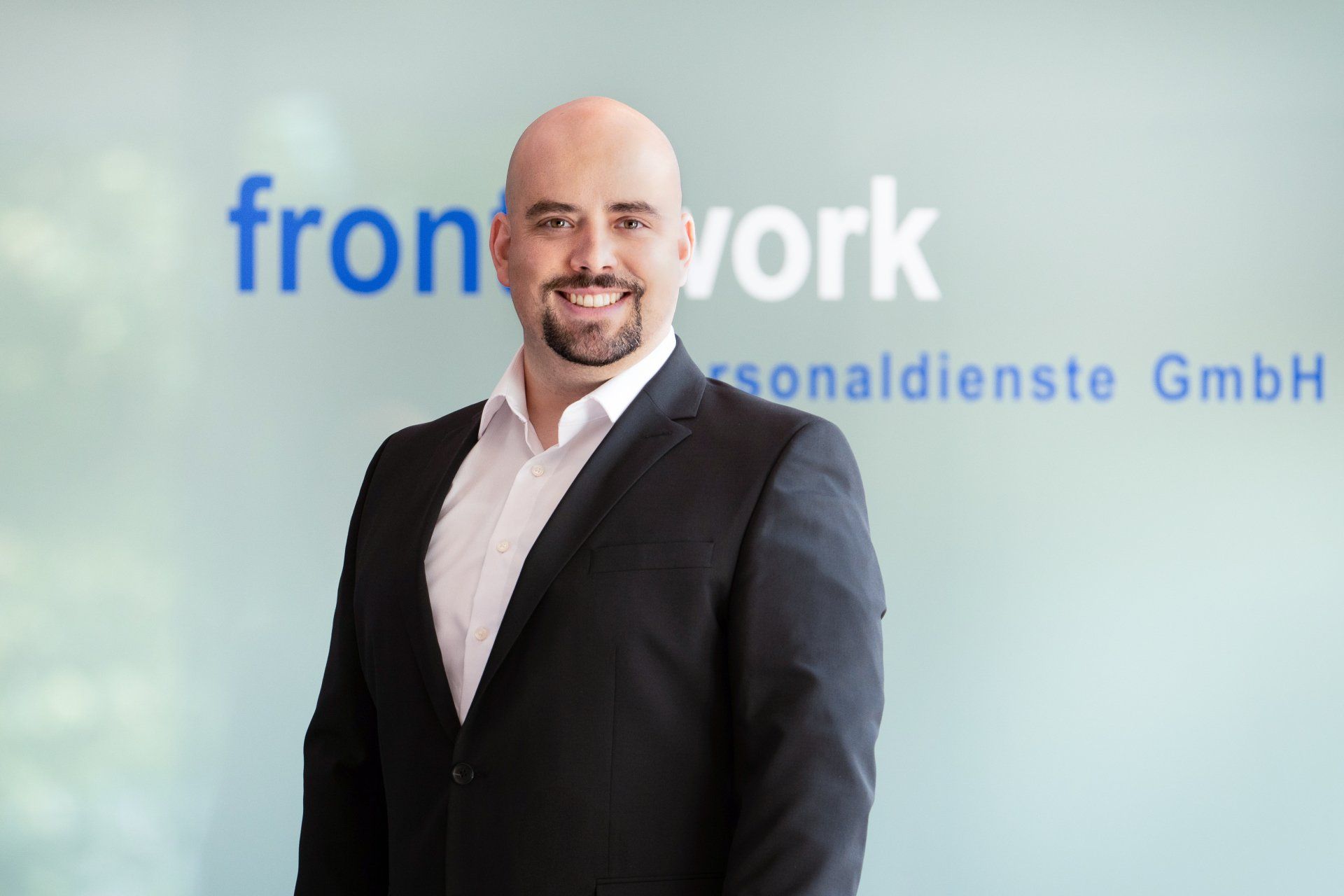 Ein Mann im Anzug steht vor einem Schild mit der Aufschrift „Frontwork“