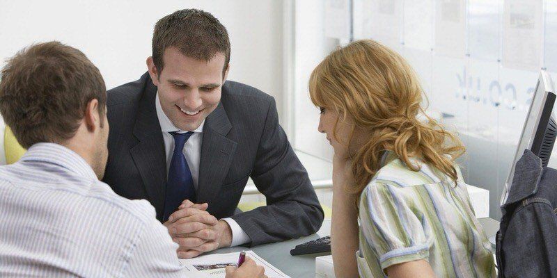 Three coworkers in business attire meeting and smiling around a desk in an office