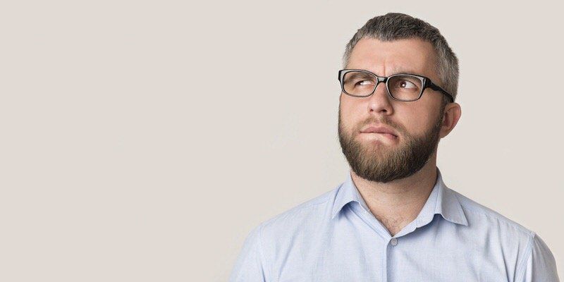 Bearded man in glasses wearing a light blue shirt, looking upward against a plain background