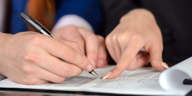 Two people point and write on a document with a pen during a meeting