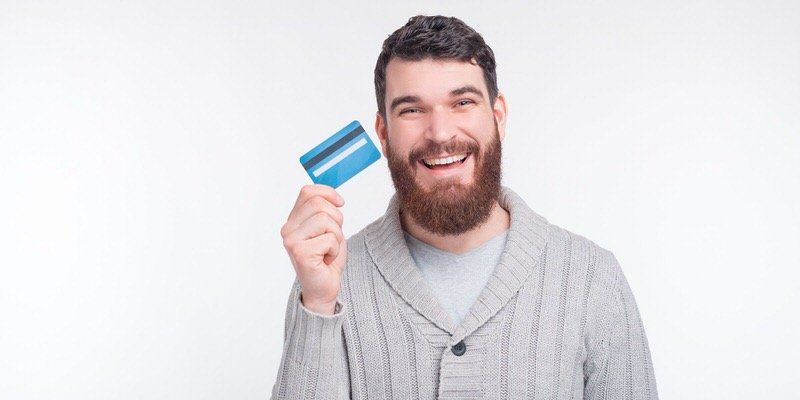 Smiling man holding a blue credit card against a light background