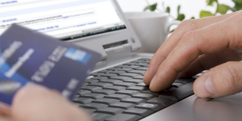 Hand typing on a laptop with a credit card nearby, suggesting online shopping