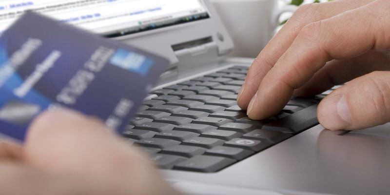 Hand typing on laptop keyboard while holding a blue credit card