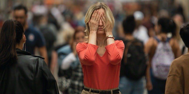 Woman in red top covers her face in a crowded public space, looking distressed