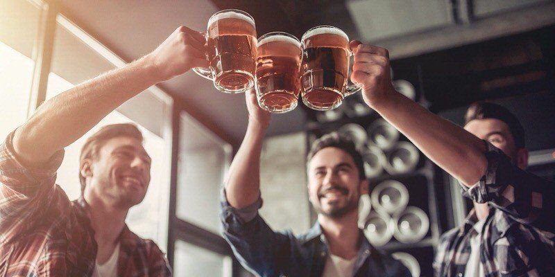 Three people clink beer mugs together in a cheerful bar setting