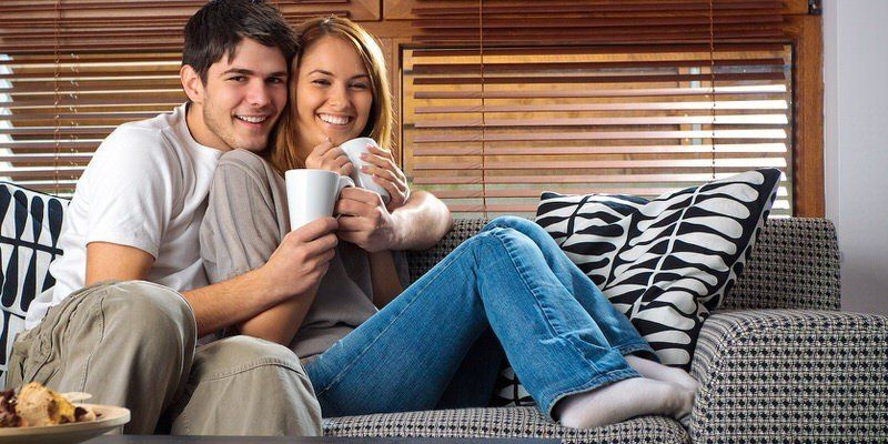 Couple relaxing on a couch, smiling and holding mugs in a bright living room