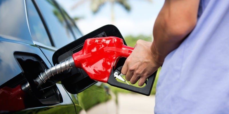 Person refueling a black car with a red gas nozzle at a gas station