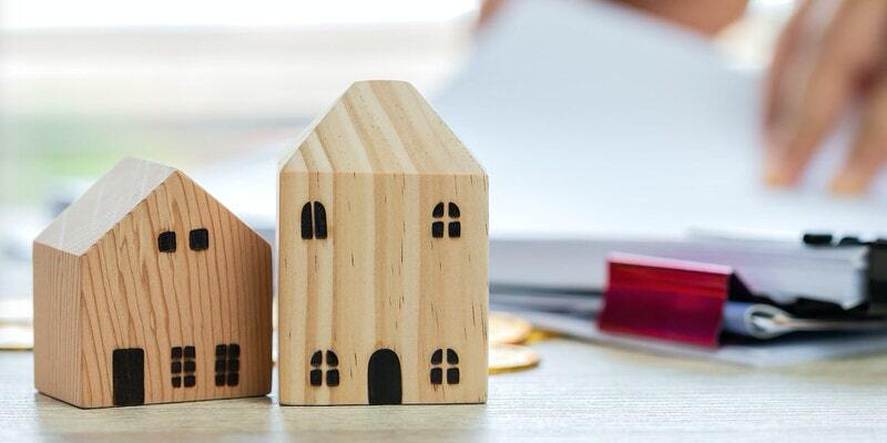 Two wooden house models on a desk beside a red pen and blurred hands in the background