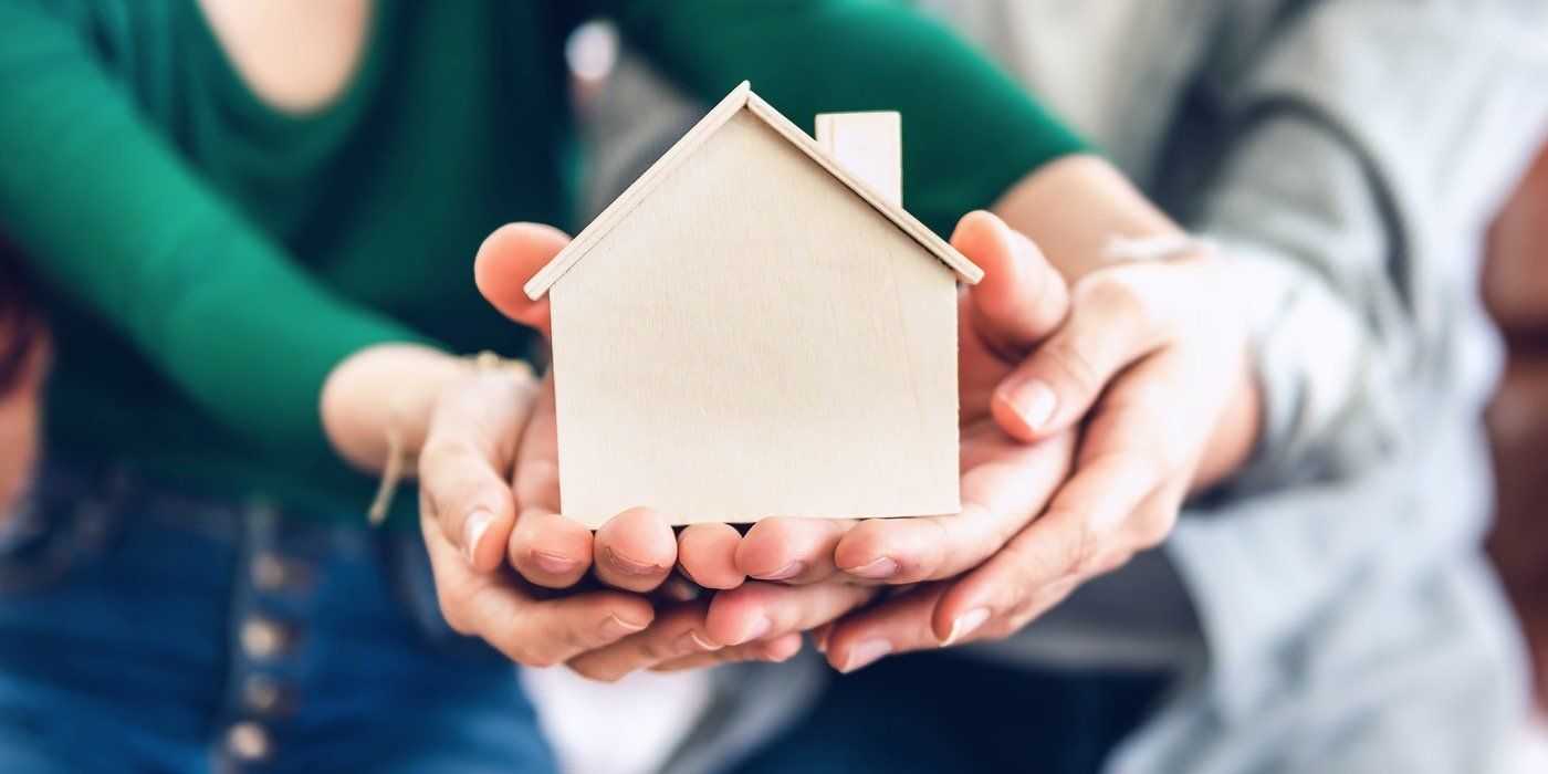 Hands holding a small white house model against a blurred background