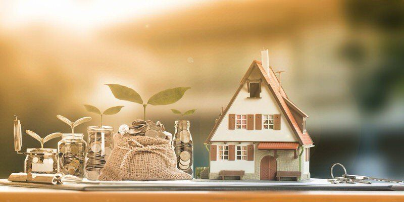 Miniature house, plant sprouts, and money jar on a table at sunrise, symbolizing savings and growth