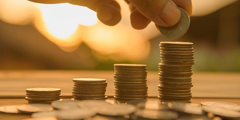 Hand stacking coins into growing piles on a table with warm sunlight in the background