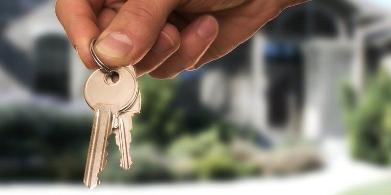 Hand holding a set of house keys in front of a blurred home exterior
