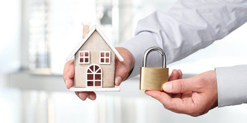 Hands holding a house model and a brass padlock, symbolizing home security or property protection