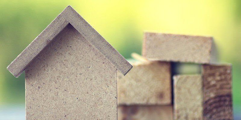 Small wooden house blocks stacked on a light background with a blurred green backdrop