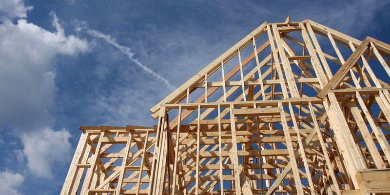 Wooden house frame under construction against a cloudy blue sky