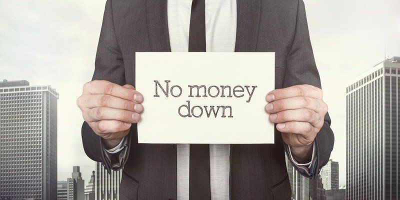 Person in suit holding a sign that reads “No money down” in front of city buildings.