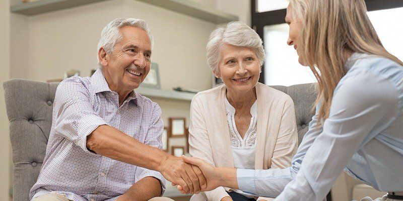 Two smiling people shaking hands with a woman in a bright living room