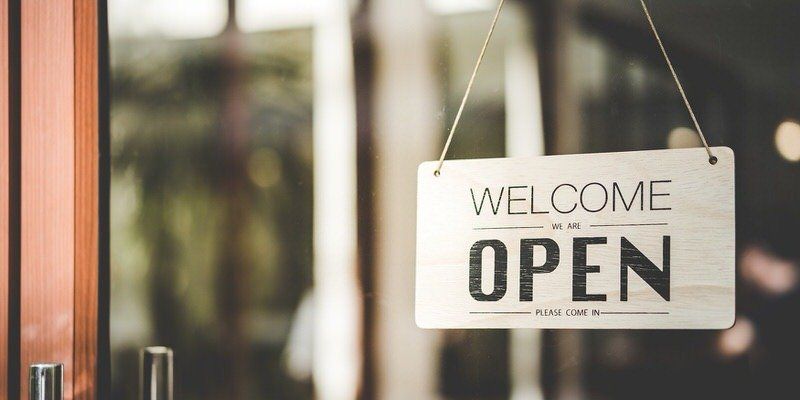 “OPEN” sign hanging in a doorway beside a welcome plaque