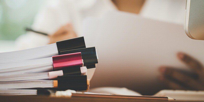 Stack of notebooks and pens on a desk with a blurred person working in the background