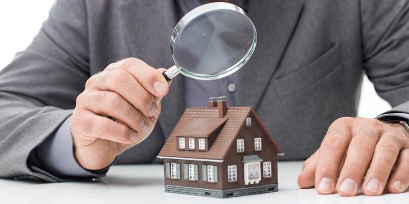 Hand holding a magnifying glass over a small house model on a desk