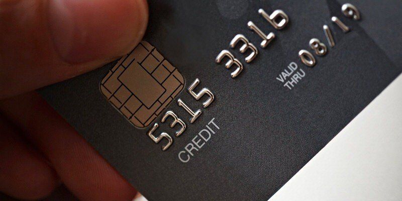 Close-up of a black credit card with embossed numbers and a hand holding it