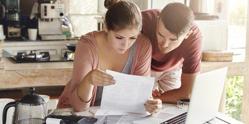 Two people reviewing paperwork together in a bright kitchen, one pointing at a document