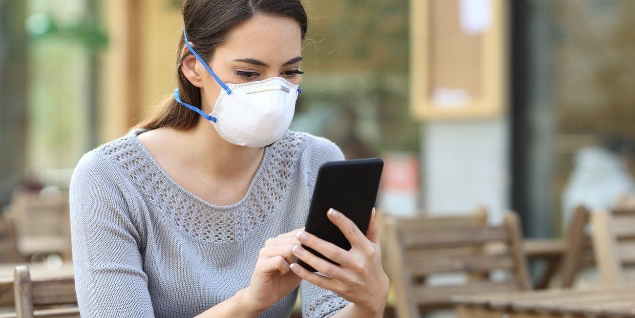 Person wearing a face mask using a smartphone outdoors at a cafe table