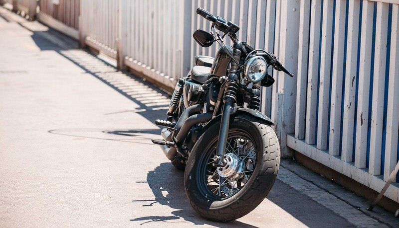 Black motorcycle parked on a sunlit sidewalk beside a white fence