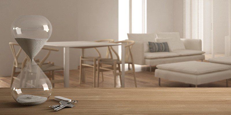 Modern living room with a sofa, dining table, hourglass, and keys on a wooden floor