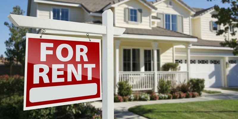 Red and white “For Rent” sign in front of a suburban house
