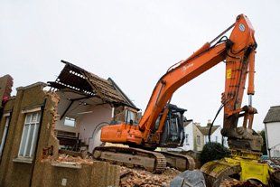 Expert demolition in Bedford, contact Bedford Demolition on 01234 340 329 Orange JCB digger knocking down house with beige bricks