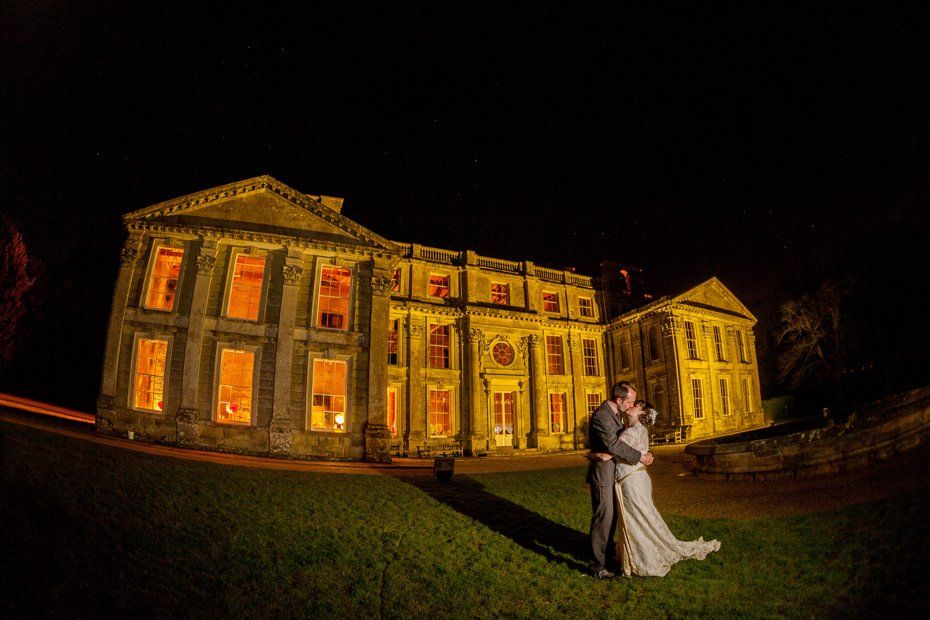 Couple embracing in front of a grand, illuminated building at night; long dress, formal attire.