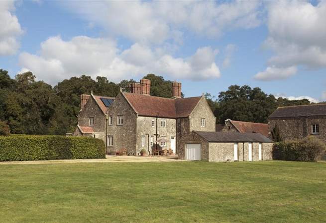 Large stone house with a red tiled roof, a lawn, and trees under a blue sky.