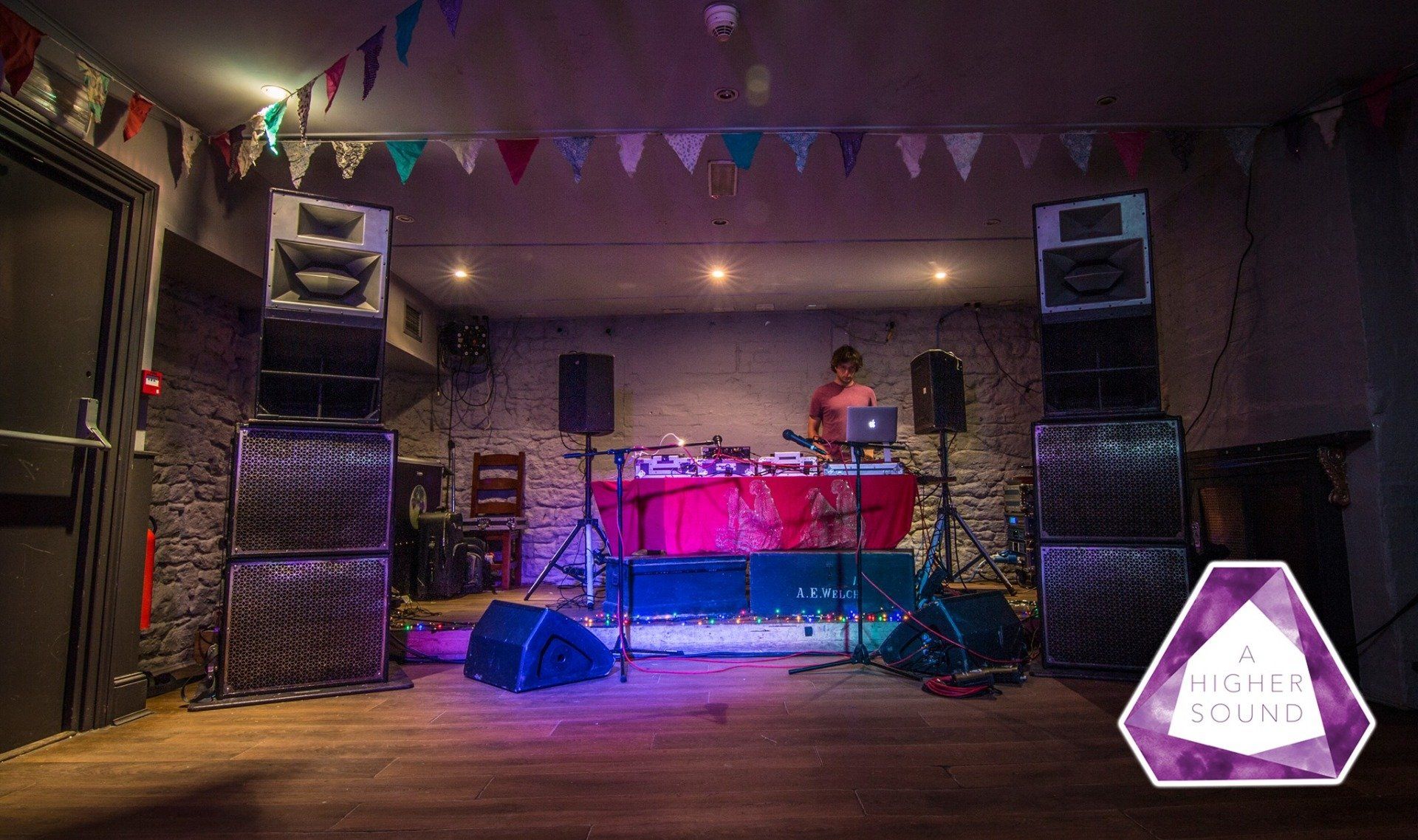 DJ at a venue with large speakers, colorful lights, and bunting.
