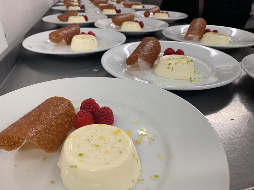 Plated desserts: Panna cotta with fruit and a crisp, in a row on a counter.