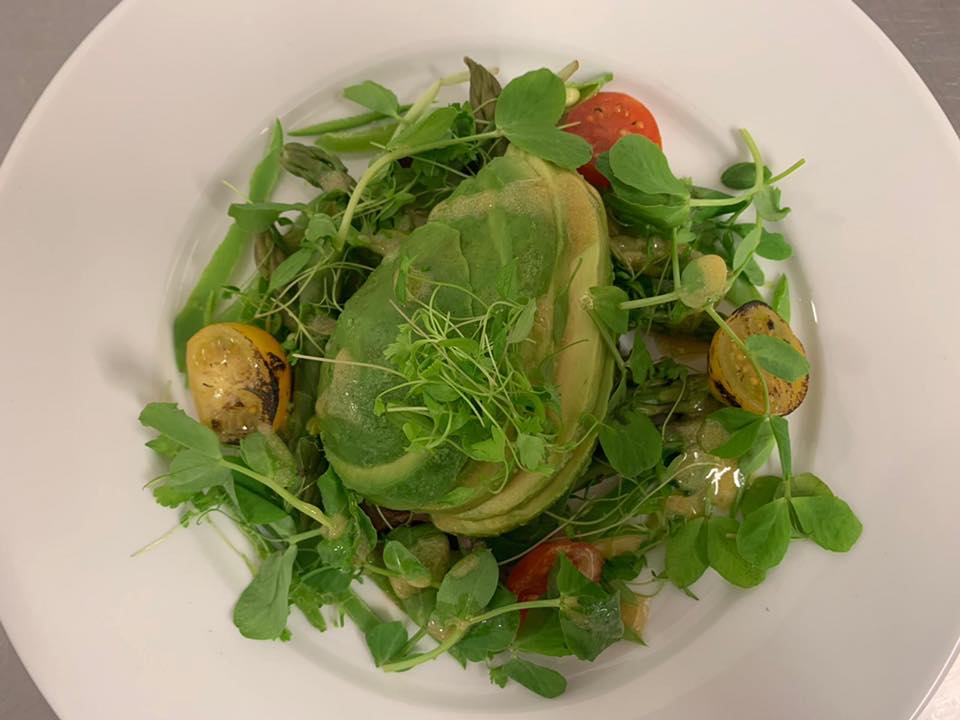 Salad with avocado slices, greens, tomatoes, and pea shoots on a white plate.