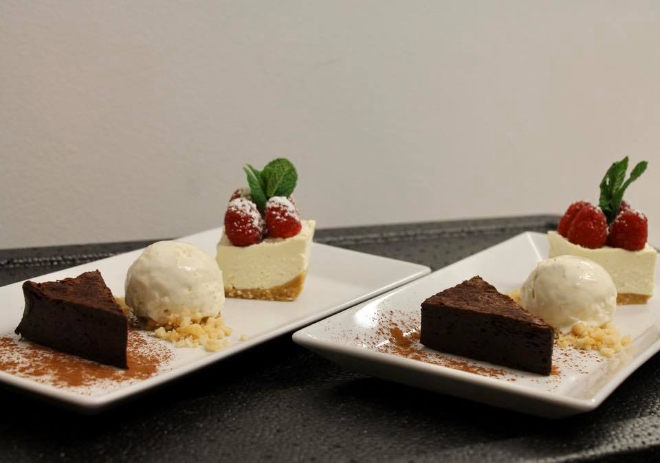 Two plates of dessert: chocolate cake, vanilla ice cream, and cheesecake topped with raspberries and mint.
