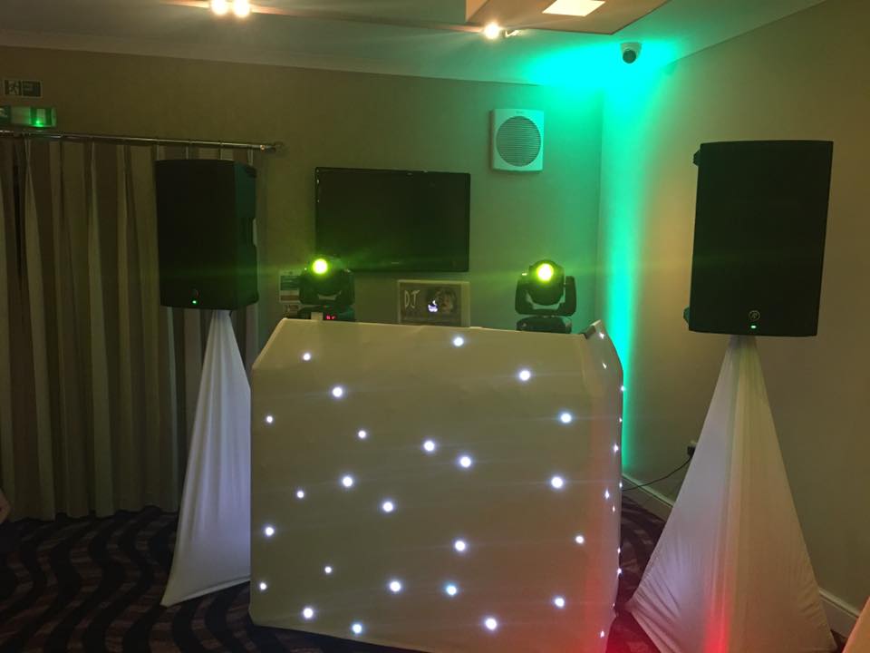 DJ setup: White, glowing DJ booth with speakers, stage lights, and fabric backdrop.