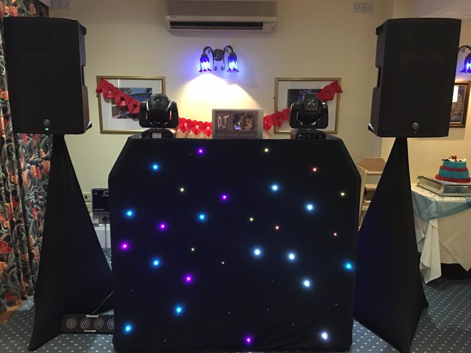DJ setup with speakers, lights, and a starry backdrop in a room.