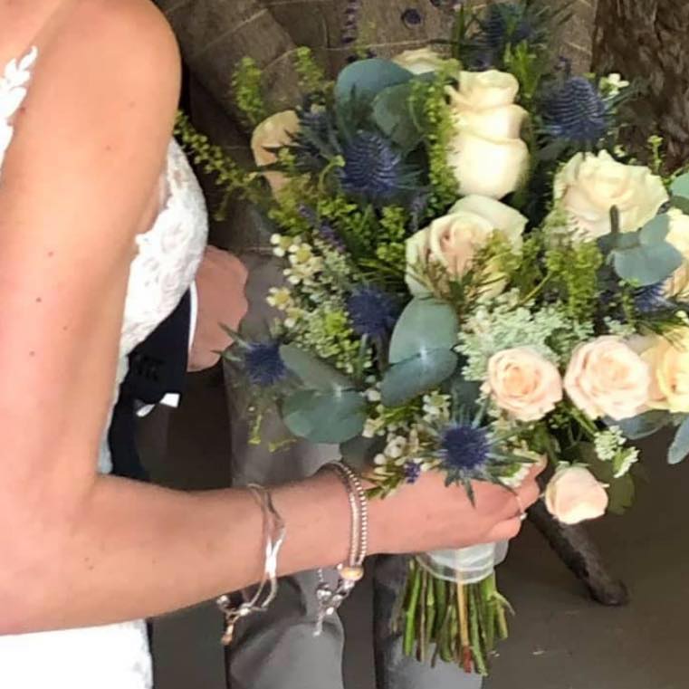 Bride holding a bouquet of cream roses, blue thistle, and greenery.