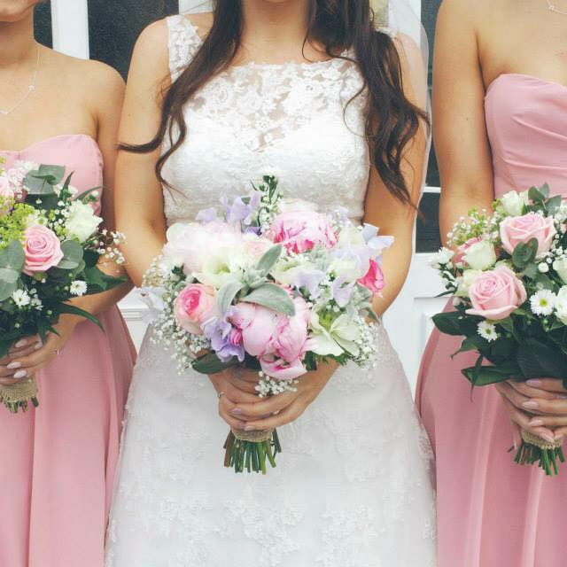 Bride in white lace dress with two bridesmaids in pink dresses, holding bouquets.