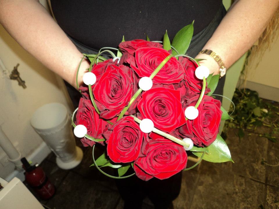 Person holding a bouquet of red roses, decorated with white spheres and green accents.