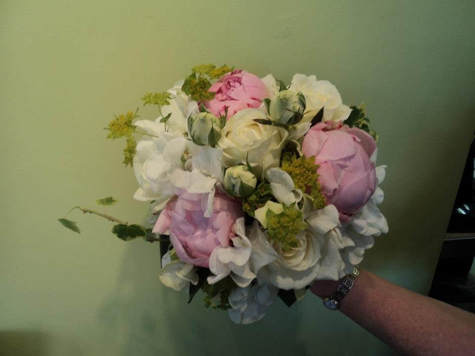 Bouquet of pink and white peonies and greenery held against a green wall.