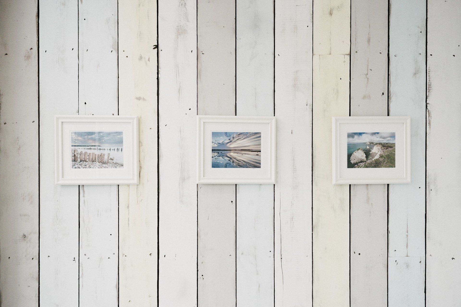 Three framed landscape photos on a white, weathered wooden wall.
