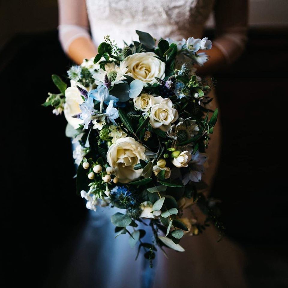 Bride holding a cascading bouquet of white roses and blue flowers.